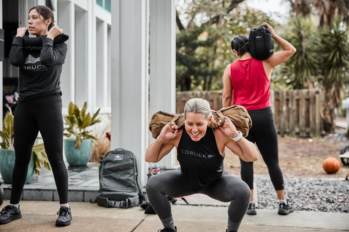 Women training outdoors with GORUCK sandbags and backpacks, doing rucking workouts