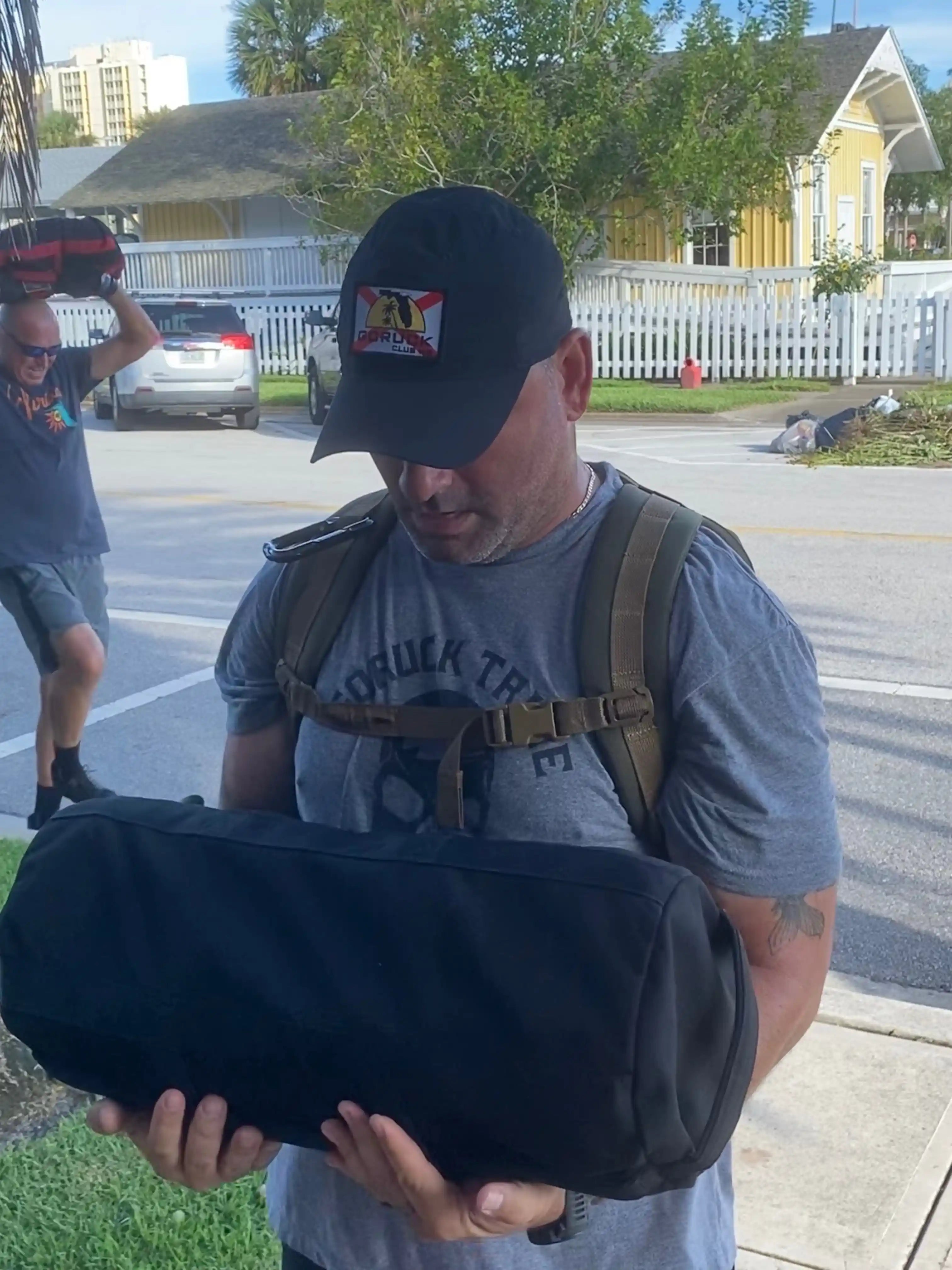 Man wearing GORUCK Tribe shirt and GORUCK Club hat carrying ruck sack outdoors