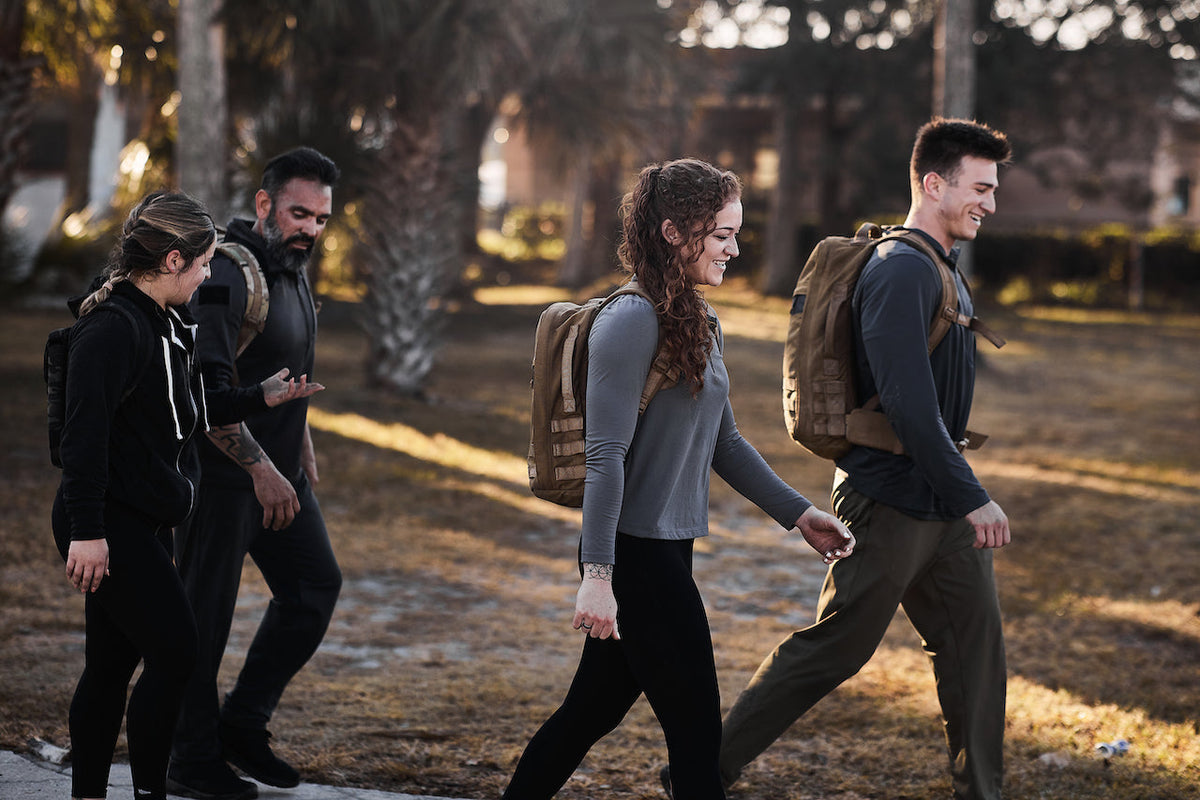 Group of people rucking outdoors with GORUCK backpacks, smiling during fitness walk