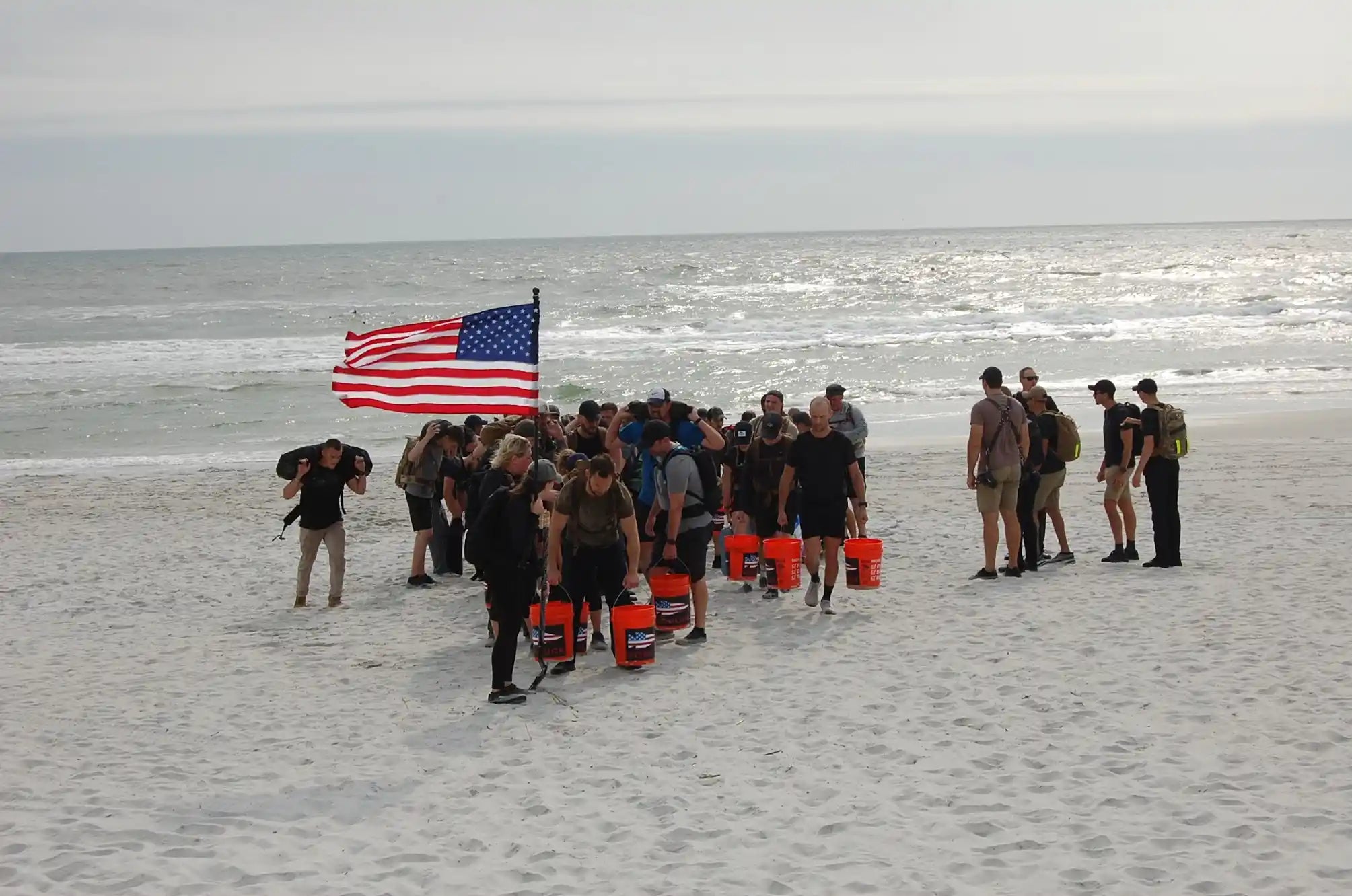 GORUCK group rucking on beach with American flag and orange buckets
