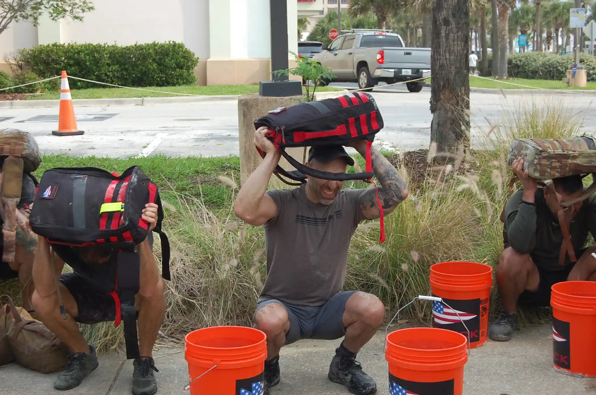 Group of people squatting outdoors with GORUCK rucksacks over their heads during a fitness event