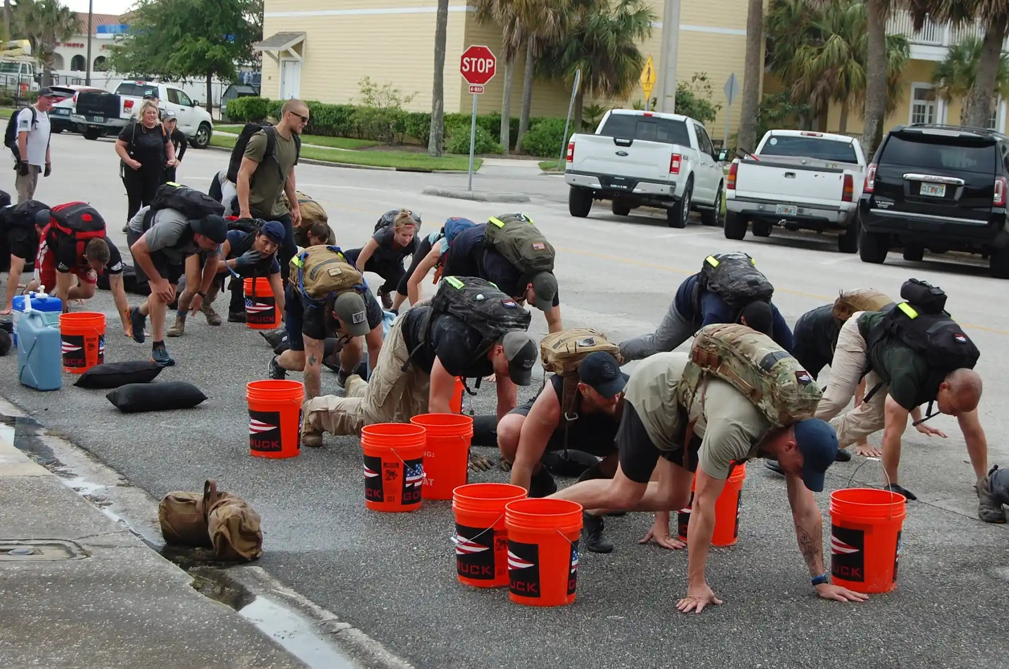 GORUCK event participants wearing rucksacks, crawling outdoors with orange GORUCK buckets