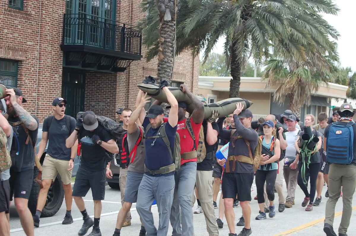 Group rucking event with participants carrying sandbags, wearing GORUCK gear outdoors
