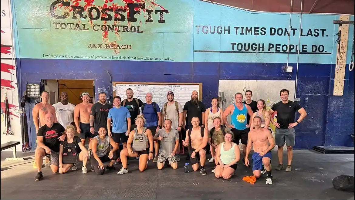 Group of athletes posing inside CrossFit gym under 'Tough times don't last. Tough people do.' mural