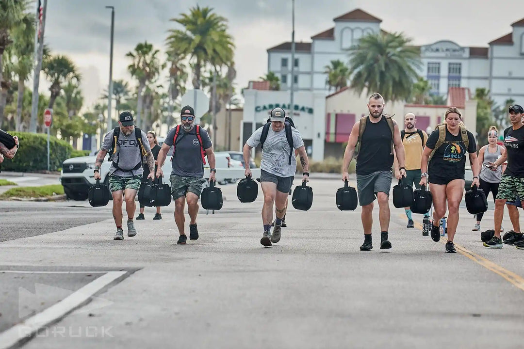 Group of people rucking outdoors with GORUCK gear, carrying weighted sandbags in city setting