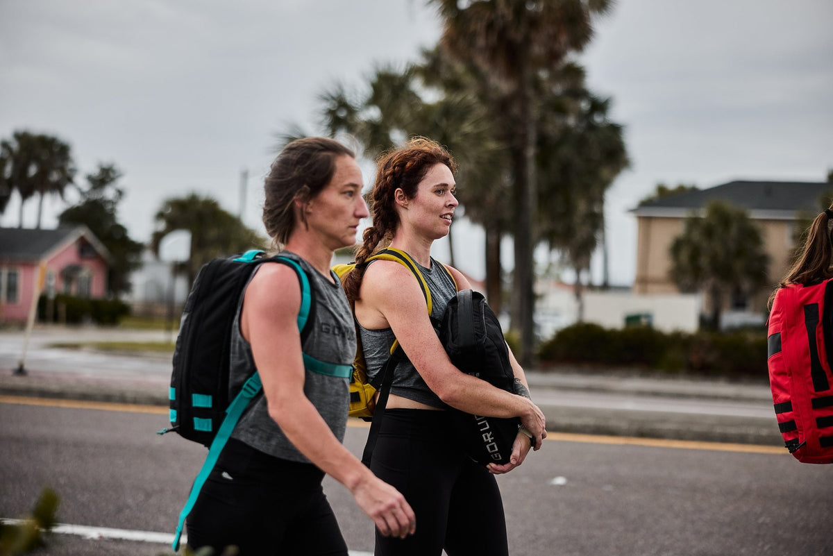 Women rucking outdoors with GORUCK backpacks, wearing athletic gear, urban palm tree background