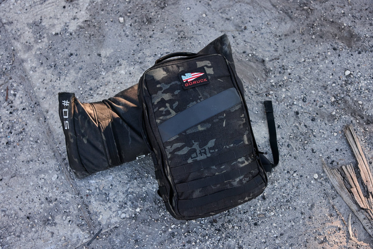 GORUCK black camo rucksack and 50 lb sandbag on rugged outdoor ground
