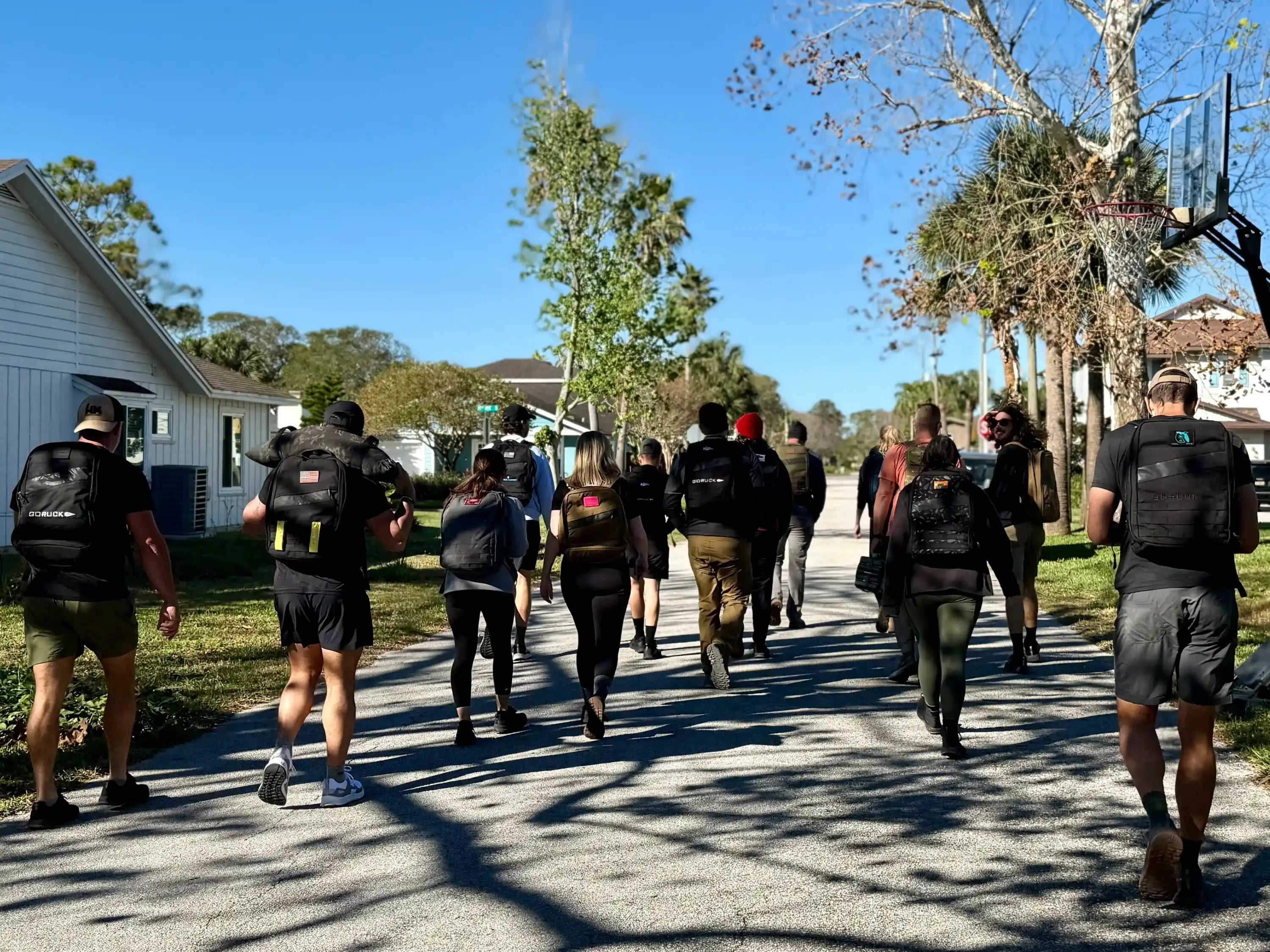Group of people rucking outdoors with GORUCK backpacks on a sunny neighborhood street