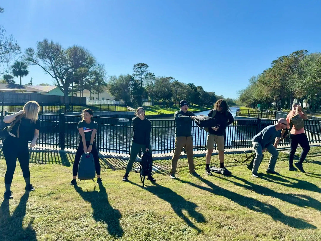 GORUCK group rucking workout outdoors by a canal, participants lifting rucksacks