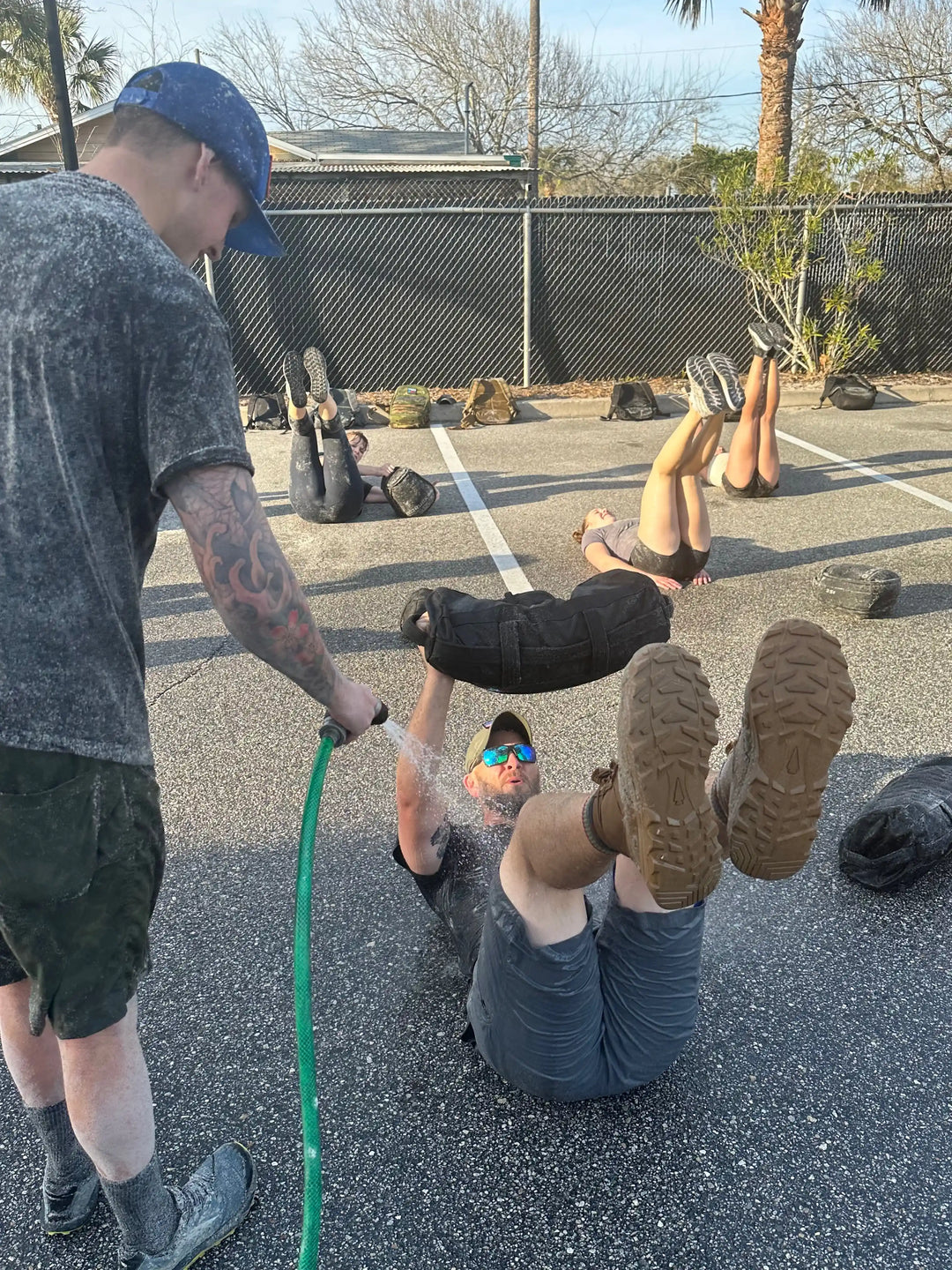 GORUCK outdoor rucking workout, participants on ground lifting sandbags, water sprayed, training gear visible