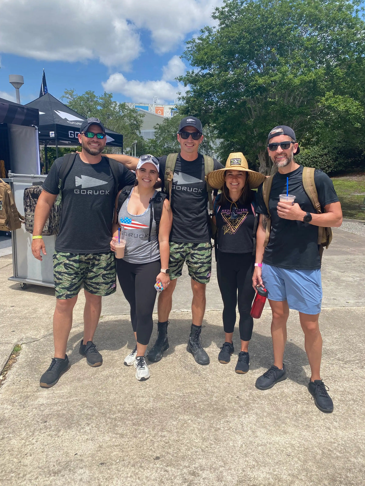 Group of people in GORUCK gear smiling outdoors at an event, with branded tent and backpacks.
