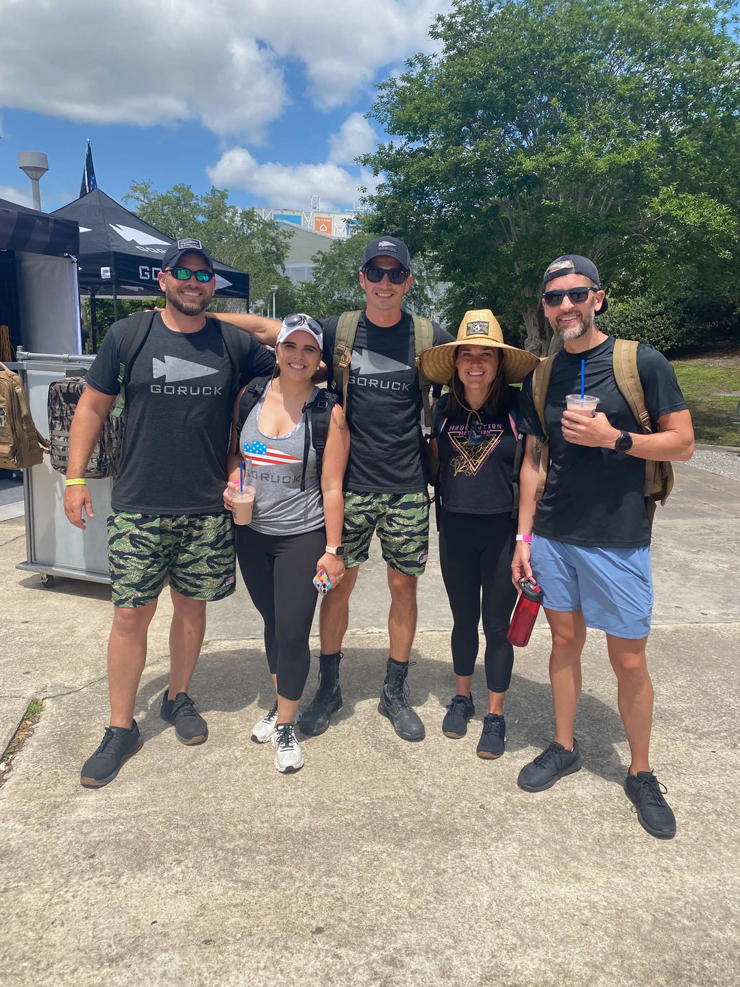 Group of five people in GORUCK gear outdoors at an event, with tents and trees in background