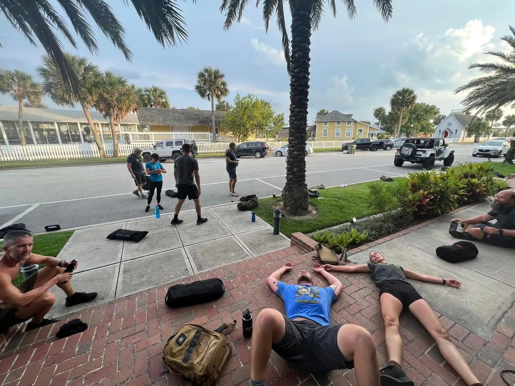 GORUCK participants resting on sidewalk after outdoor rucking workout, gear beside them