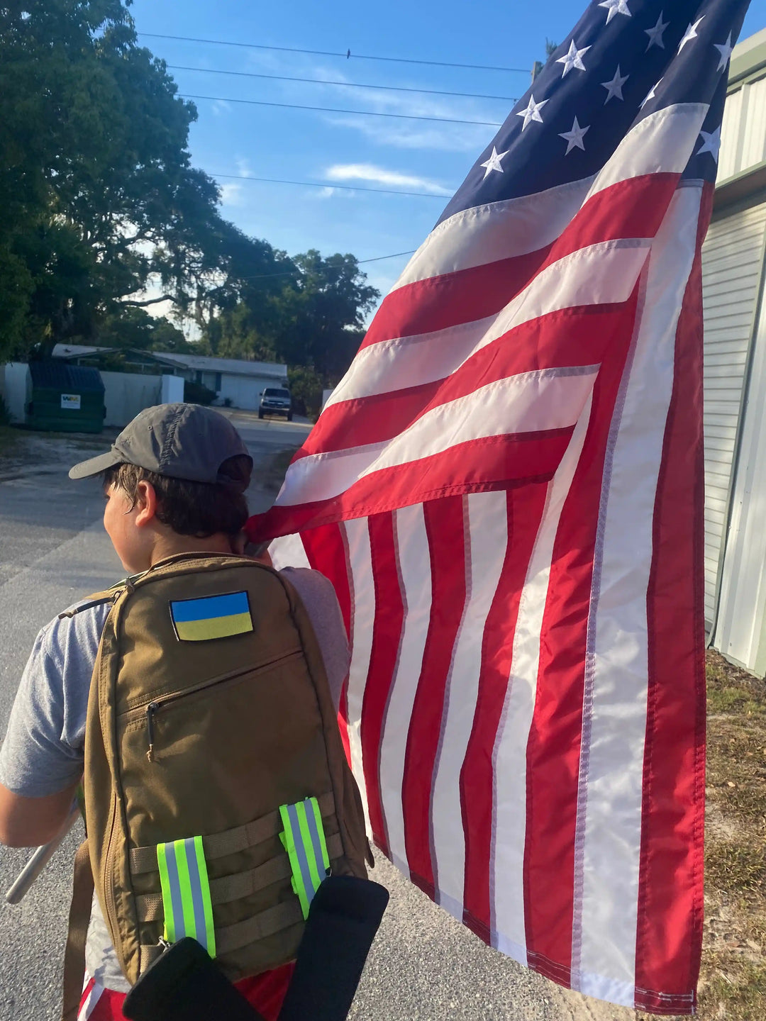Person rucking with a GORUCK backpack and carrying an American flag outdoors