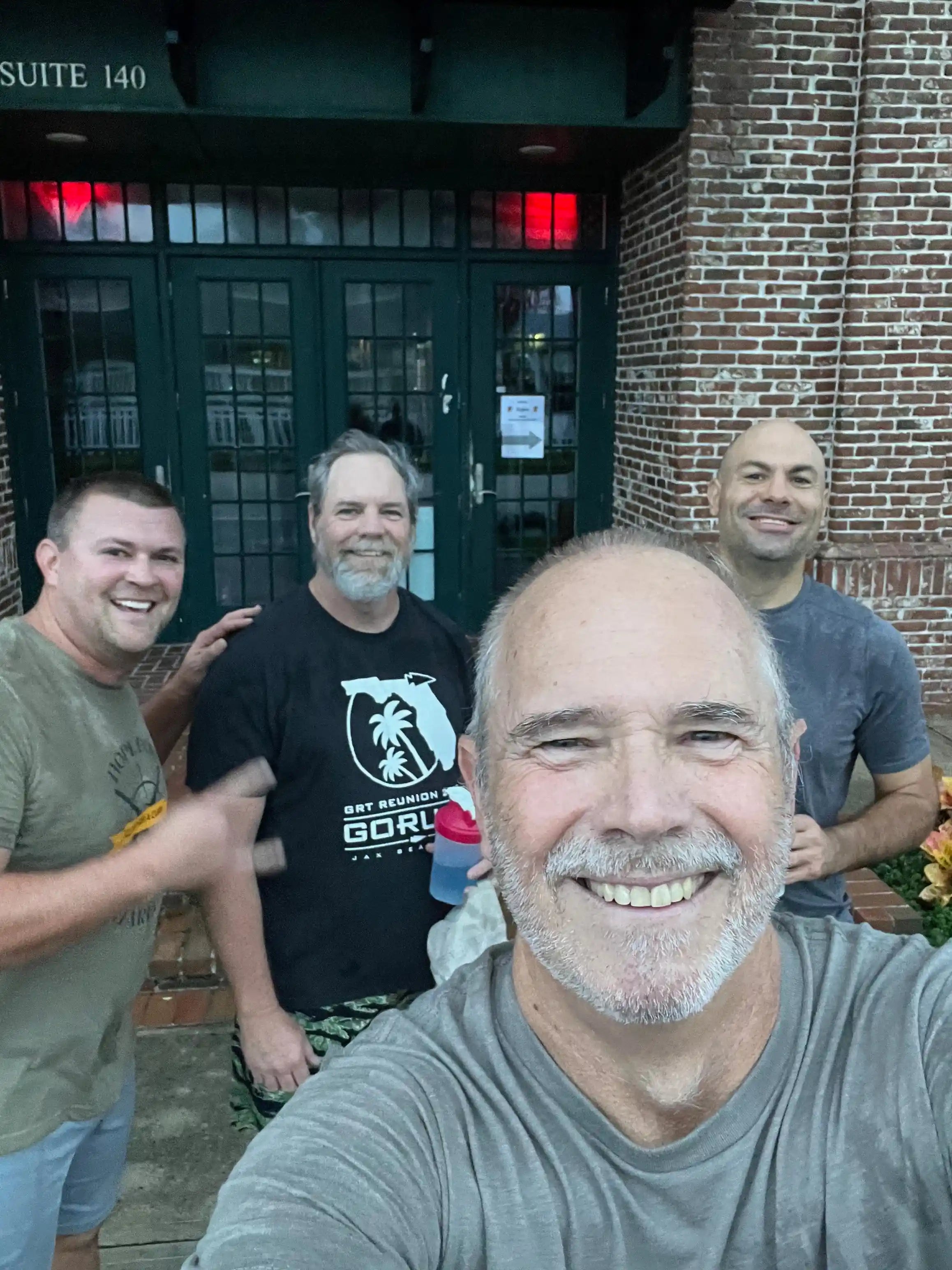 Group of smiling men outside brick building, one wearing GORUCK shirt, post-ruck event