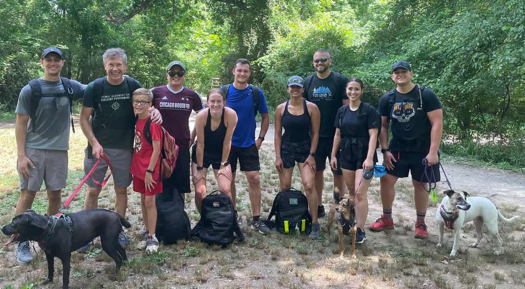 Group of people with dogs wearing rucking gear outdoors, GORUCK community event in nature