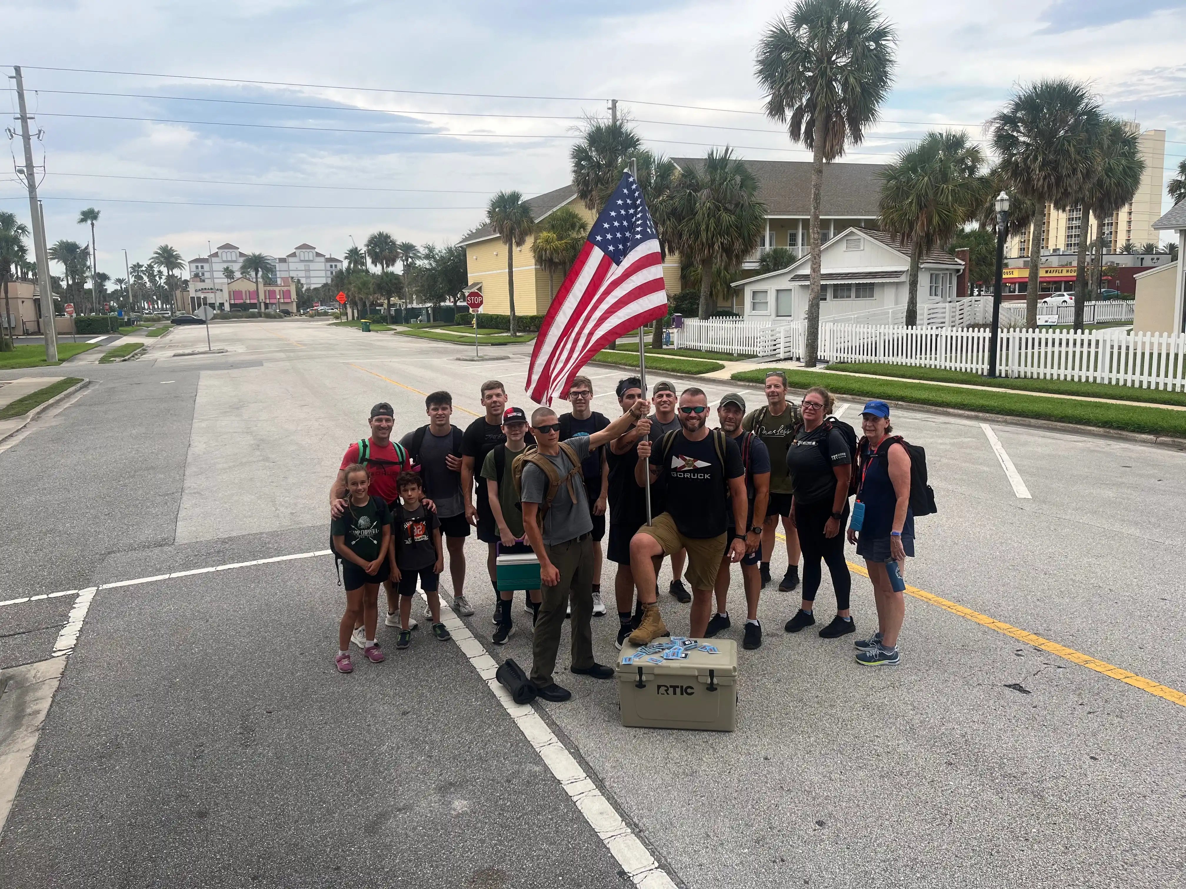 Group of people with GORUCK gear holding American flag on city street, palm trees in background