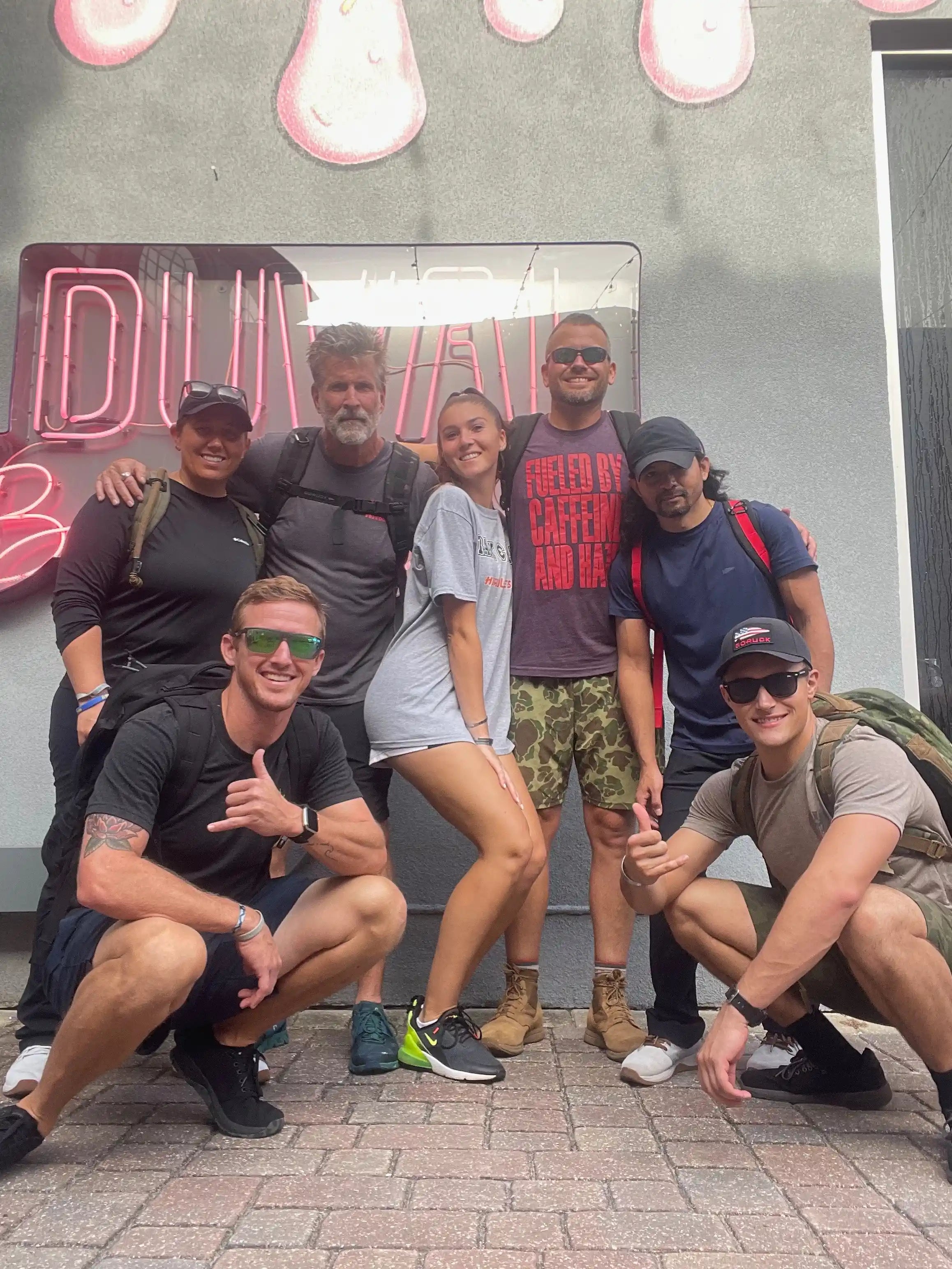 Group of people in athletic gear with GORUCK backpacks posing outside under neon Duval sign