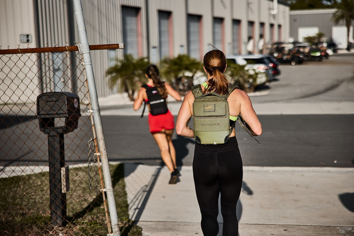 Women rucking with GORUCK backpacks outside industrial buildings on a sunny day