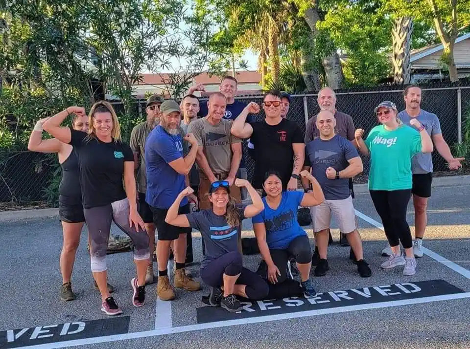 GORUCK community group posing outdoors, flexing arms in athletic gear at a rucking event