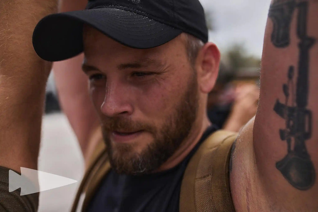 Man wearing black cap and rucksack training outdoors at GORUCK rucking event, close-up view.