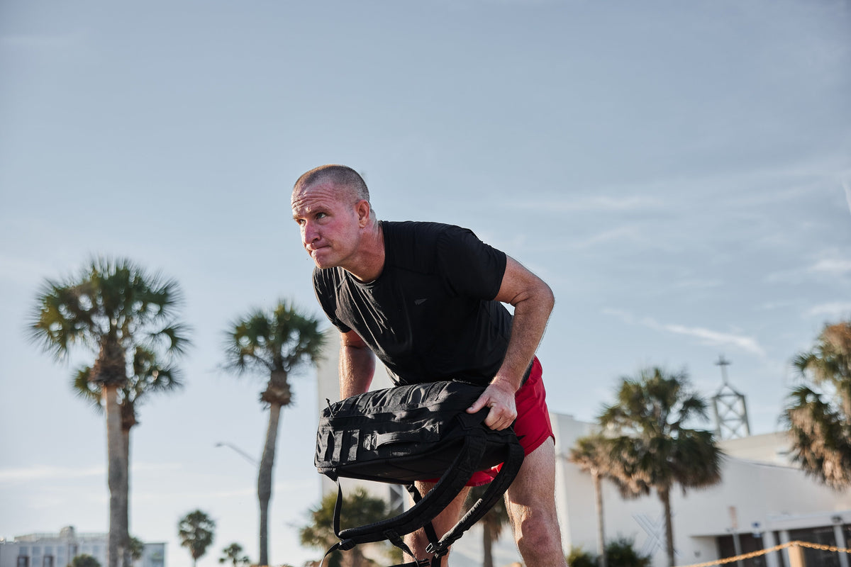 Man rucking outdoors with GORUCK backpack, palm trees in background, fitness activity