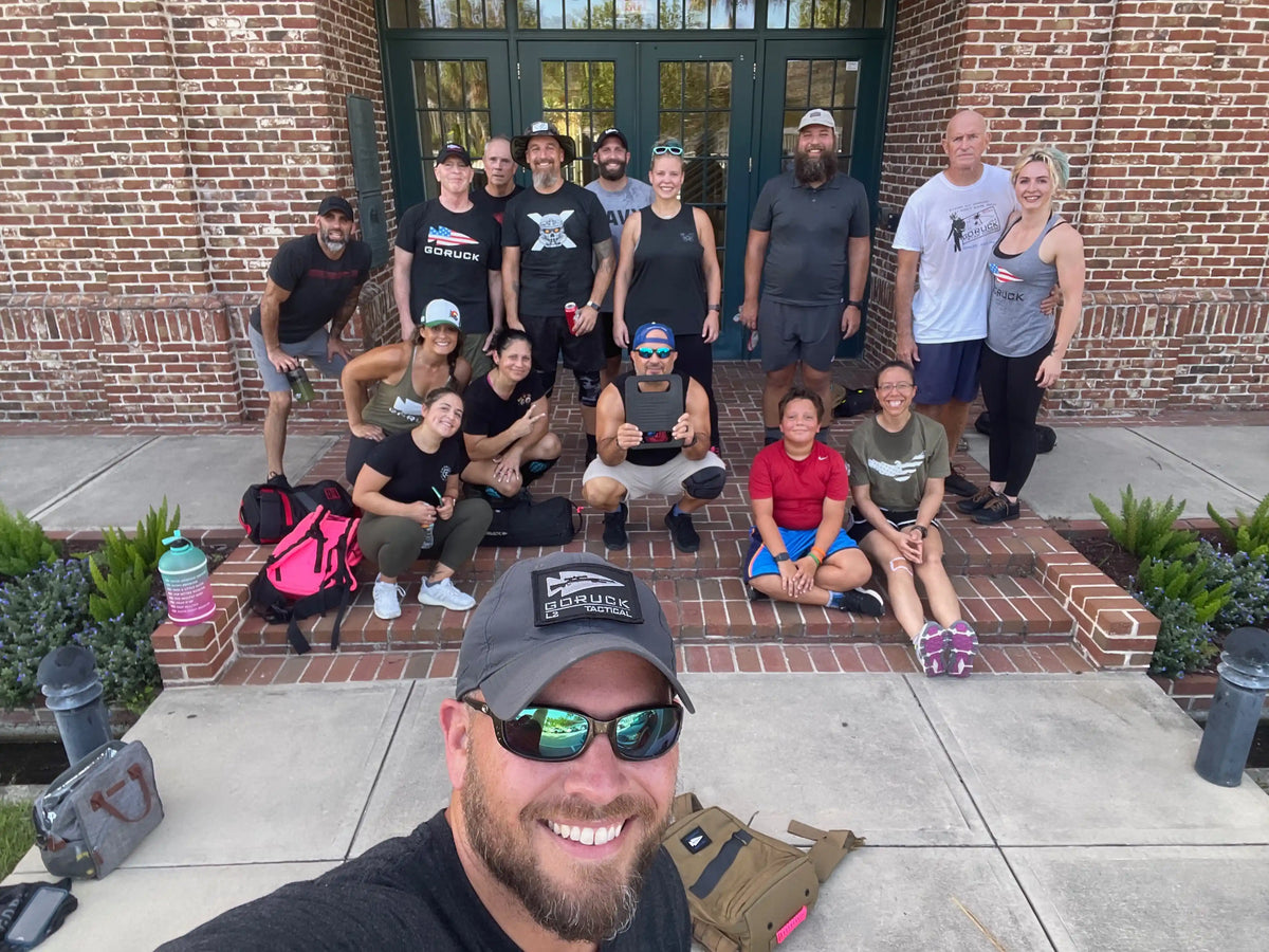 GORUCK group selfie with rucking gear outside brick building, smiling after event