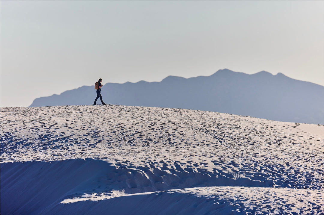Person rucking with backpack on sandy dune, mountains in background, GORUCK outdoor gear