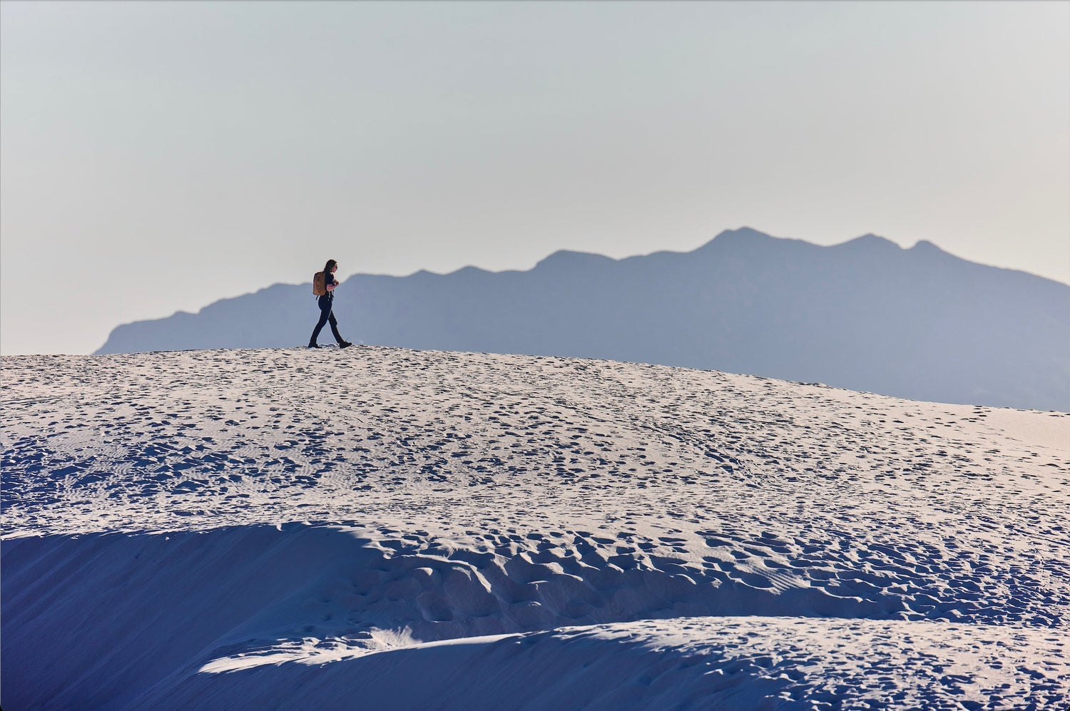 Person rucking with backpack on sandy dune, mountains in background, GORUCK outdoor gear