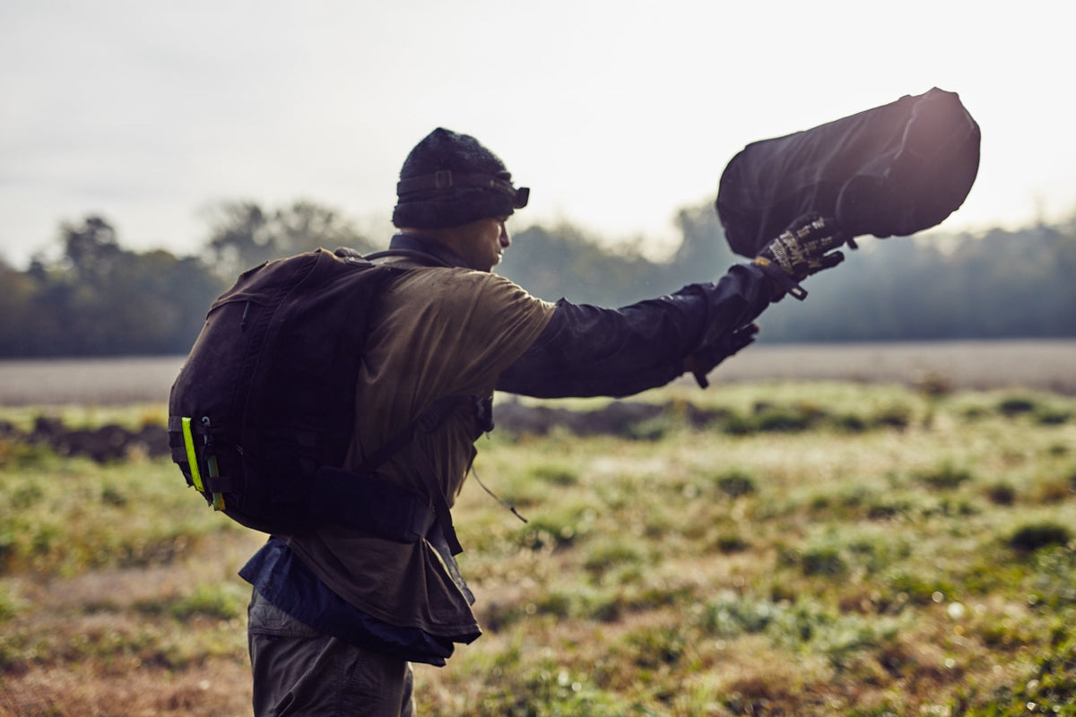 GORUCK athlete in outdoor gear rucking with backpack and sandbag in a grassy field