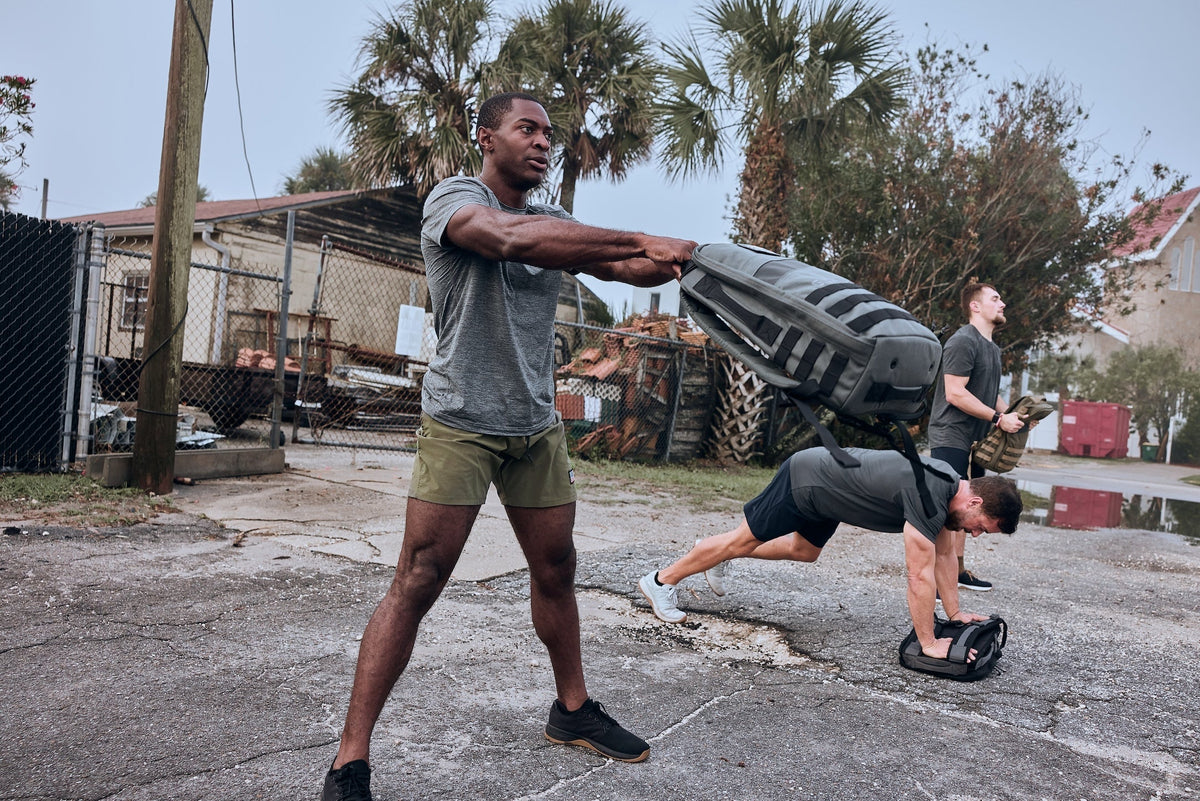 Men training outdoors with GORUCK rucksacks, performing strength and rucking exercises.