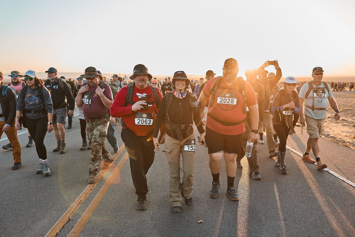 Rucking event participants wearing GORUCK gear walking on a road at sunrise in a group challenge.