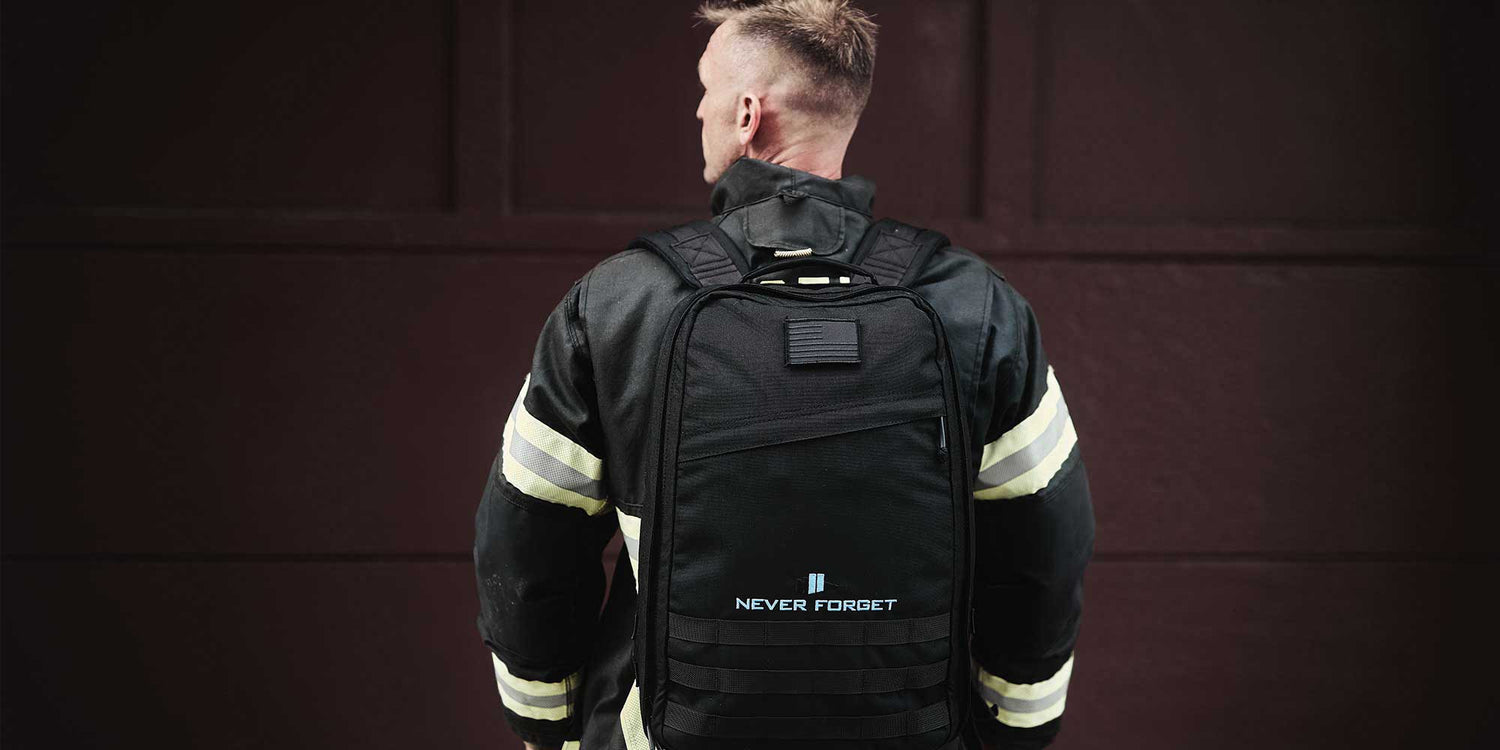 A firefighter in uniform faces away, wearing a black backpack with 