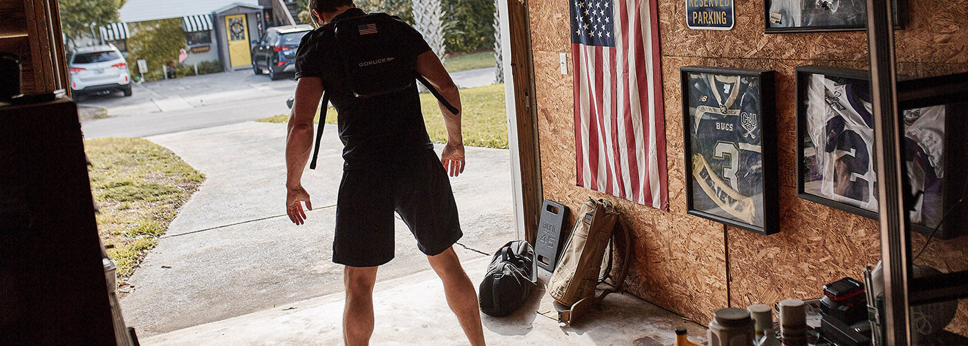 Man in athletic wear stretching in garage with American flag and sports memorabilia on the wall.