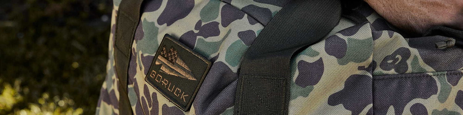 Close-up of a green camouflage backpack with a patch featuring an American flag and the text 