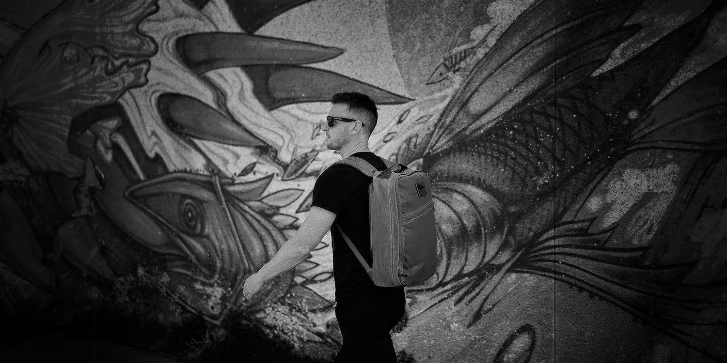 Person with a backpack walks by detailed street art featuring abstract creatures, in black and white.