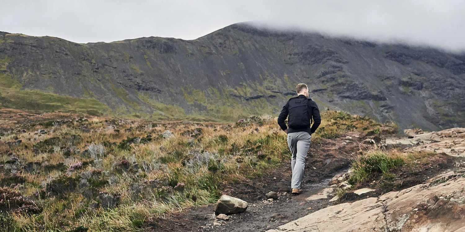 Person hiking on a rocky trail with cloudy mountains in the background.