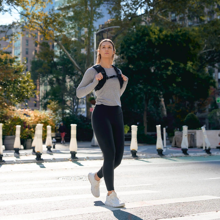 Woman rucking with GORUCK backpack, crossing city street in athletic gear, outdoor fitness