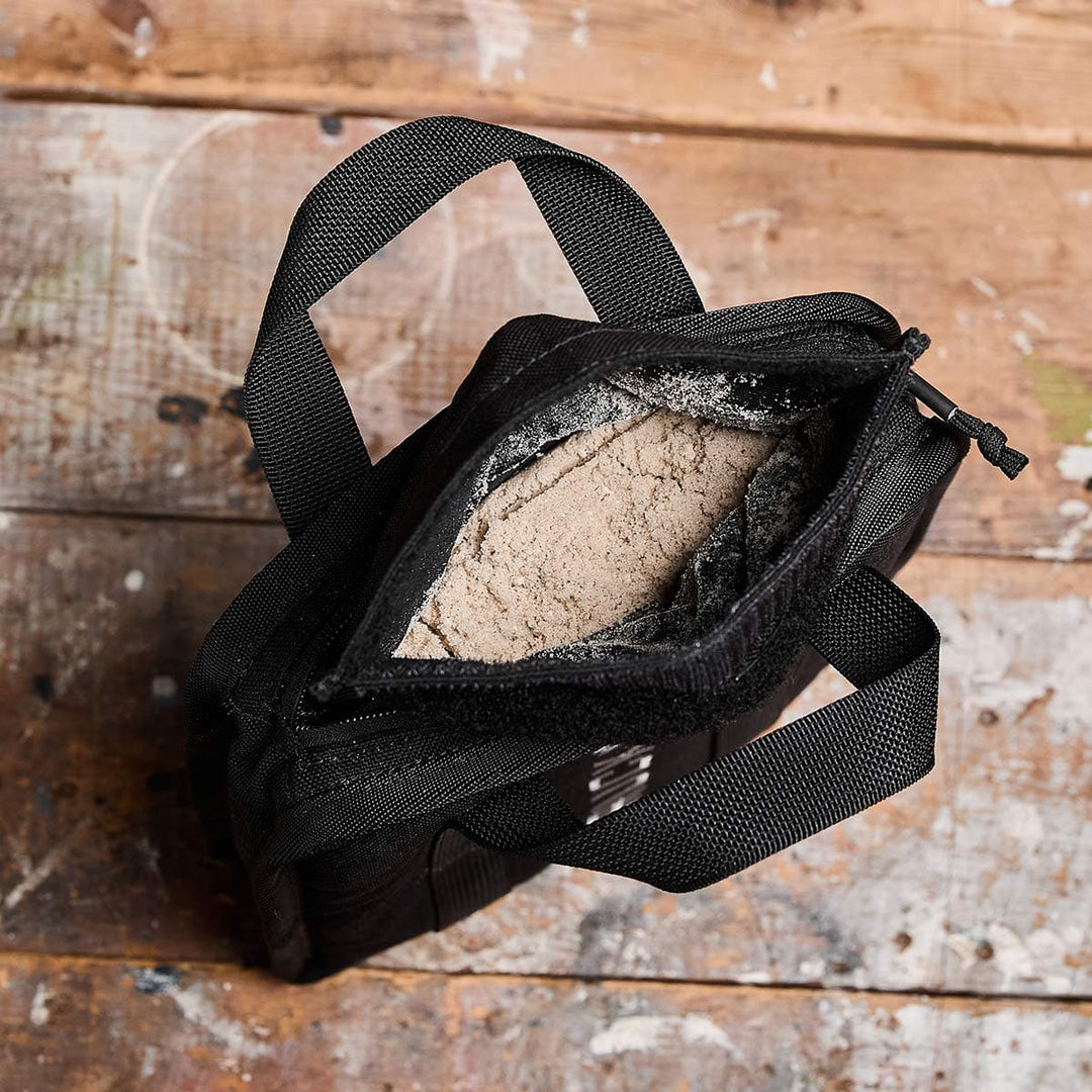 An open black bag on a wooden surface reveals a beige powder, ideal for enthusiasts of rucking with the portable Sand Ruck Plates by GORUCK.
