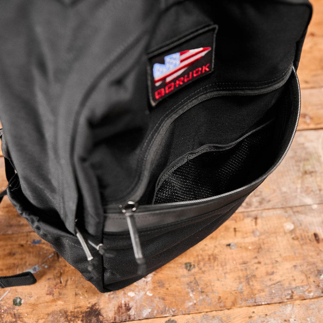 Open KR1 school backpack by GORUCK with an American flag patch, resting on a wooden surface.