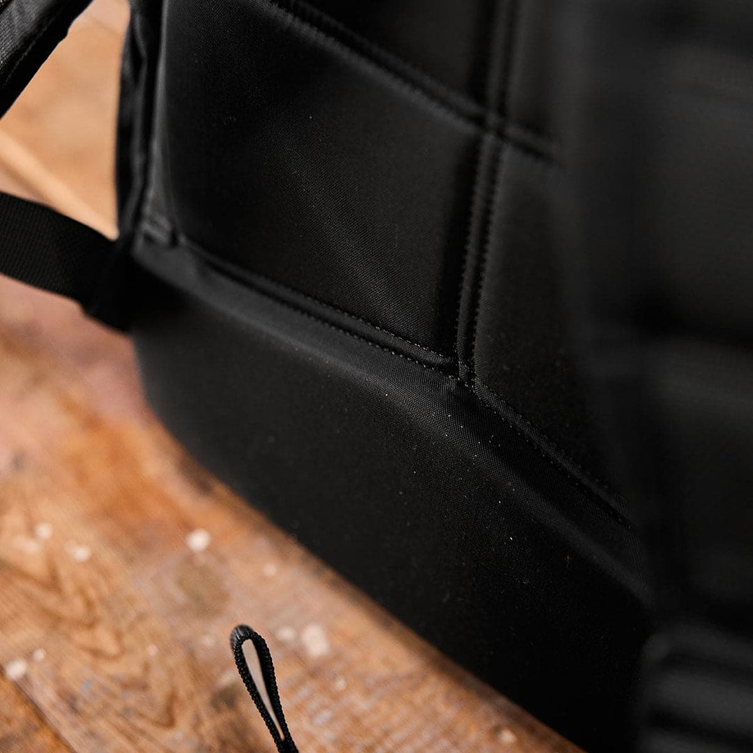 Side view of a GORUCK KR1 black backpack on a wooden surface, showcasing its stitching and strap loop, emphasizing its durability for everyday use.