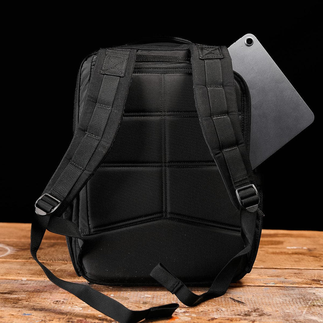 A durable KR1 backpack from GORUCK rests on a wooden surface, with a tablet partially inserted in the back pocket.