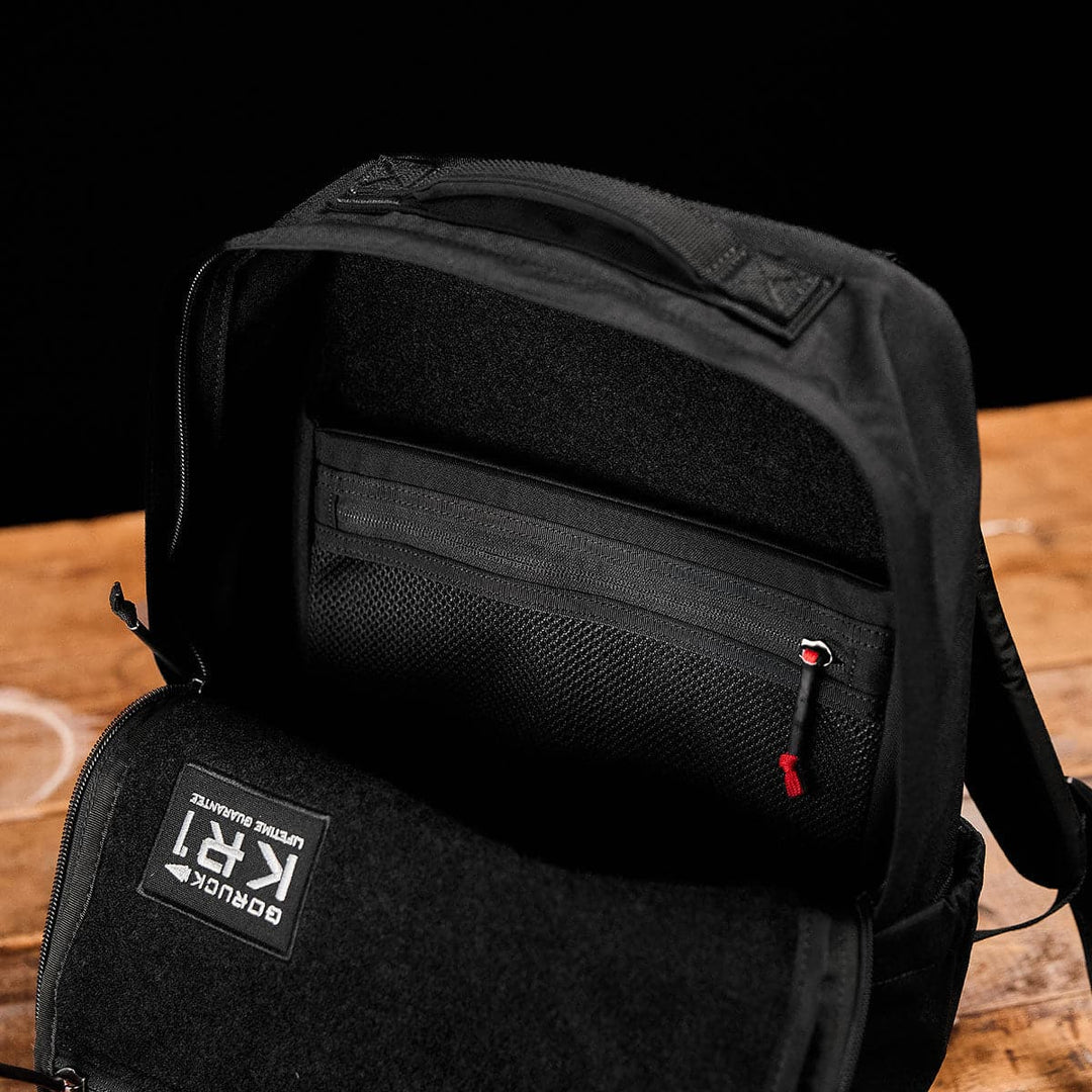 Open GORUCK KR1 black school backpack on a wooden surface, displaying inner mesh pocket and zippers.