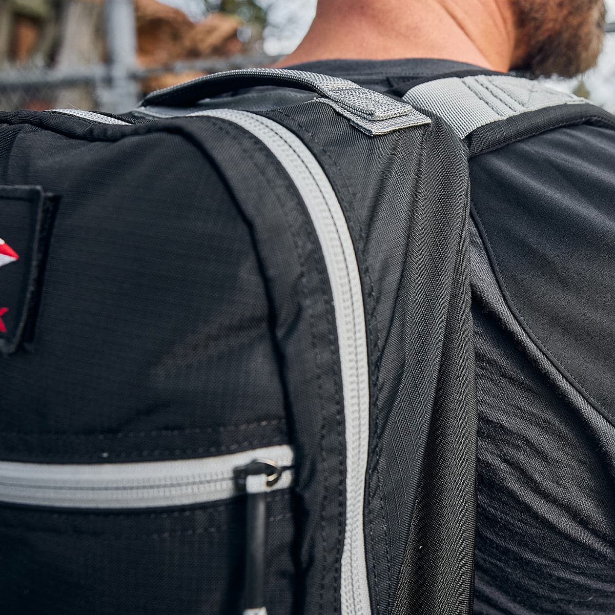 Close-up of a person wearing a black backpack with gray straps outdoors.