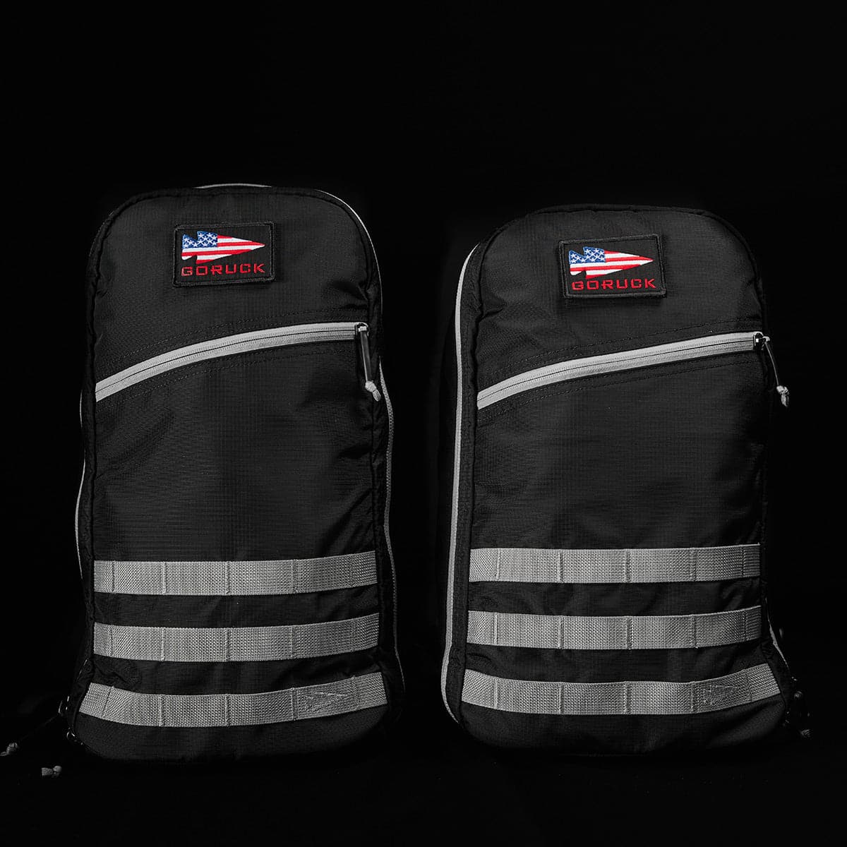 Two black GORUCK rucking backpacks with reflective stripes and American flag patches