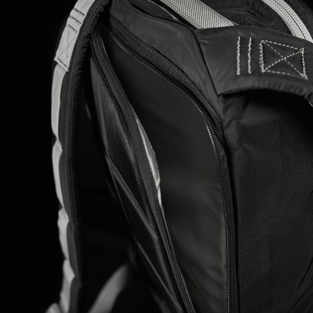 A close-up of the Bullet Ruck Laptop - Ripstop Nylon - 16L by GORUCK showcases its black design with a partially open zipper, revealing the water-resistant interior and dedicated laptop compartment, set against a dark background.