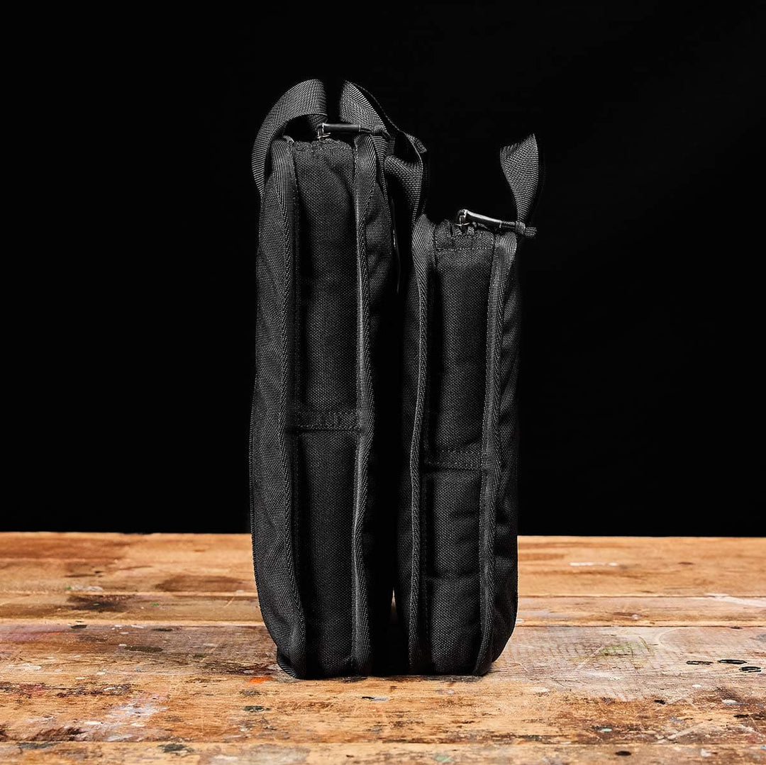 Two Sand Ruck Plates by GORUCK, each stored in black zippered pouches perfect for portability, stand upright on a wooden surface against a dark background.