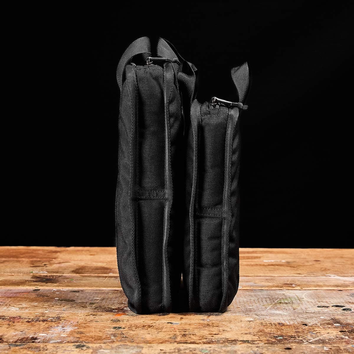 Two Sand Ruck Plates by GORUCK, each stored in black zippered pouches perfect for portability, stand upright on a wooden surface against a dark background.