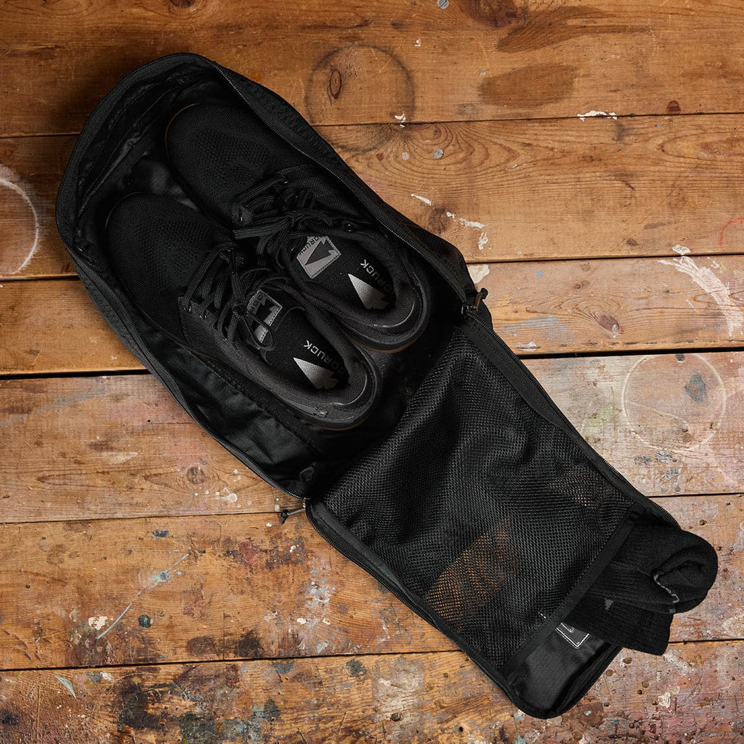 Shoes rest in a GORUCK Ripstop ROBIC shoe bag on a rustic wooden floor with paint splatters.