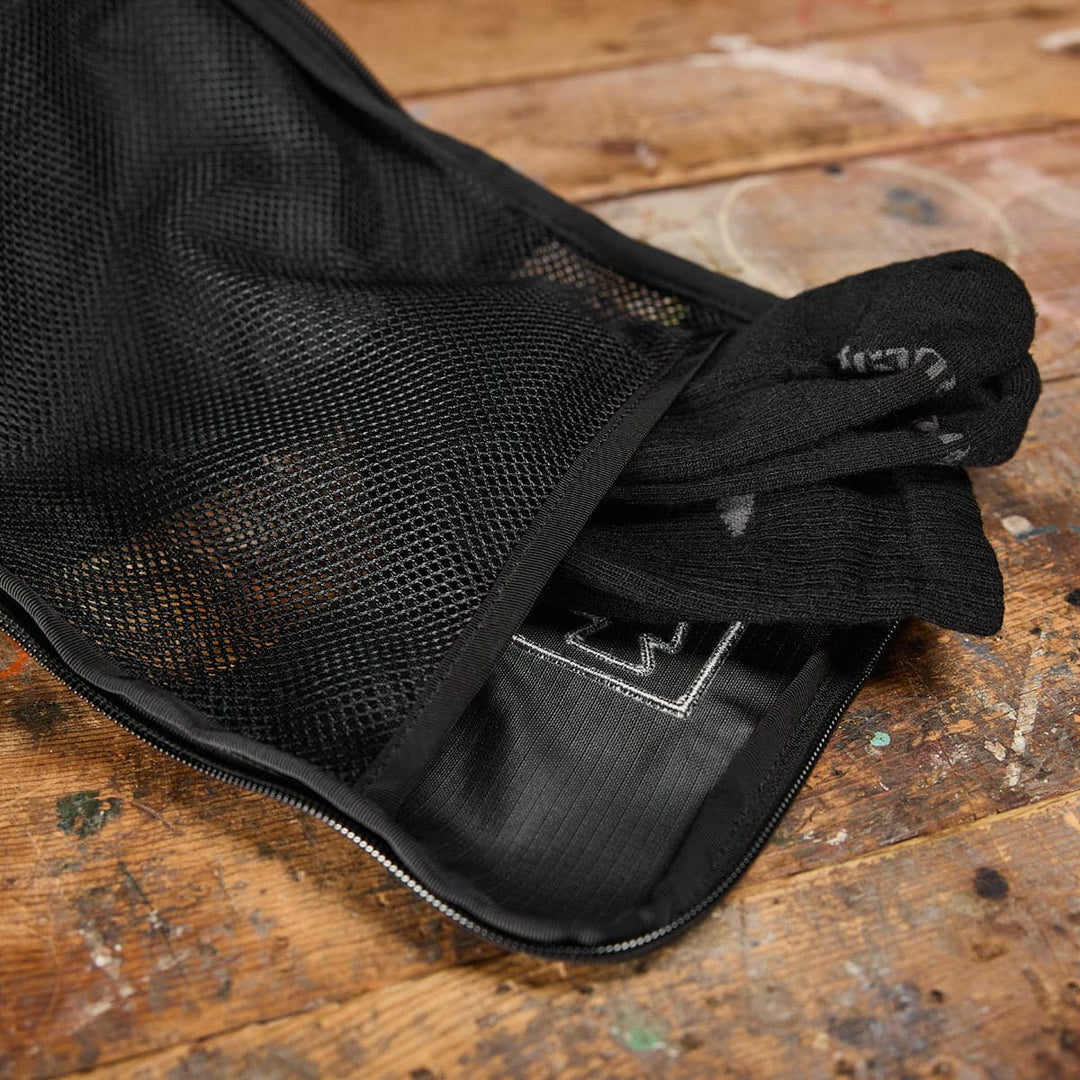 The GORUCK Shoe Bag - Ripstop ROBIC, partially open on a wooden surface, reveals black socks inside and features a black mesh design that ensures essential ventilation to keep everything fresh.